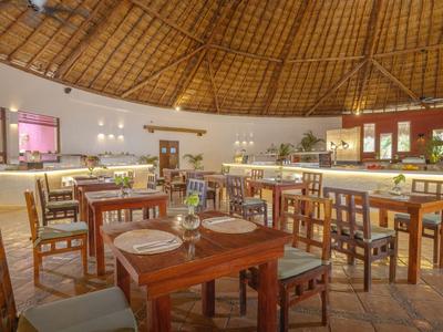 Großer Hotel-Speisesaal mit Holztischen, Stühlen und hoher, runder Strohhülle.