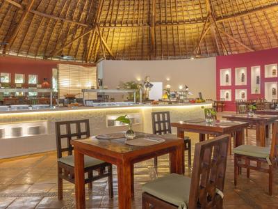 Offenes Restaurant mit Holztischen und geflochtenem Strohdach, Buffetbereich im Hintergrund.