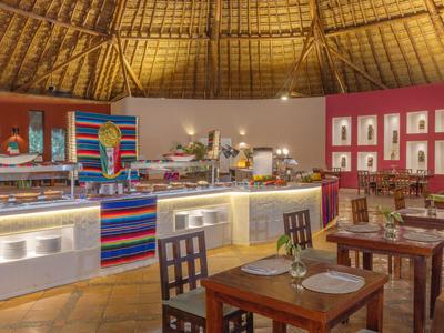 Innenbereich eines Restaurants mit Holztischen, Stühlen und Buffet in tropischer Umgebung.