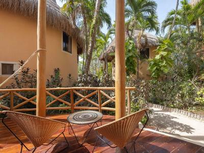 Terrasse mit zwei Holzstühlen und kleinem Metalltisch in tropischer Umgebung eines Hotels.