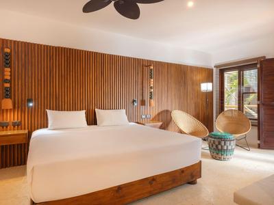 Modern eingerichtetes Hotelzimmer mit Holzwand, großem Bett und Sitzbereich neben Fenstern.