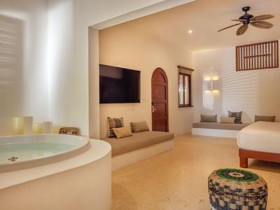 Hell eingerichtetes Hotelzimmer mit Badewanne, TV, Deckenventilator und gemütlicher Sitznische.