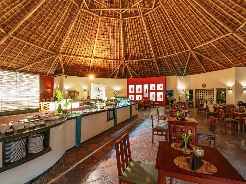 Grande salle à manger ouverte avec plafond en bois rond élevé et tables joliment dressées.