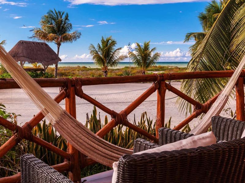 Hamac confortable et chaises sur balcon avec vue sur la mer et les palmiers.