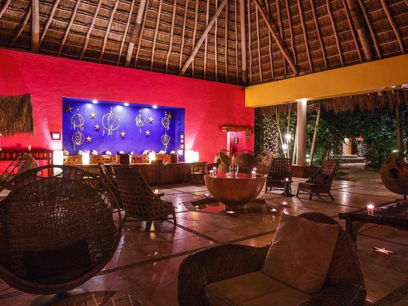 Salon d'hôtel confortable avec chaises en osier, mur rouge et plafond en bois sous toit ouvert.