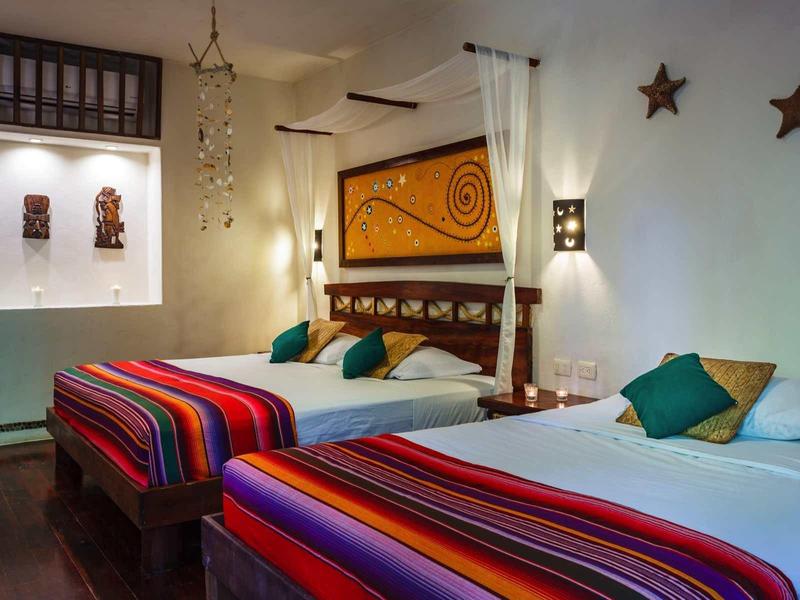 Chambre d'hôtel confortable avec deux lits, coussins colorés et étoiles décoratives au mur.