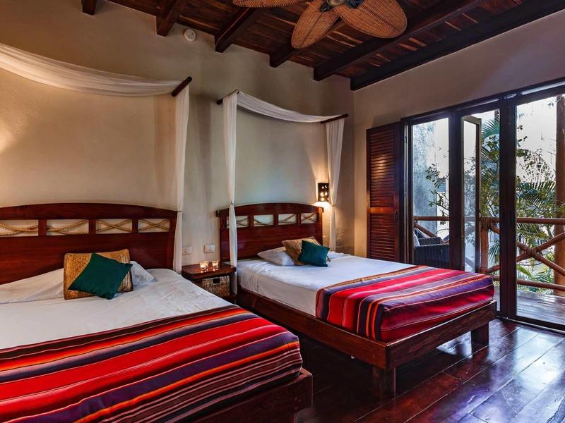 Chambre d'hôtel confortable avec deux lits, mobilier en bois et balcon donnant sur la verdure.