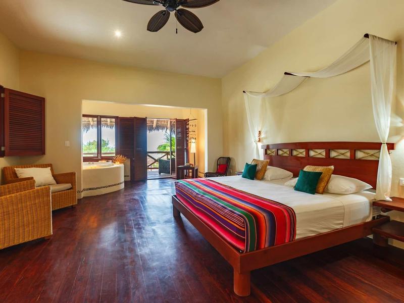 Chambre spacieuse avec sol en bois, lit double et coin salon donnant sur la terrasse.