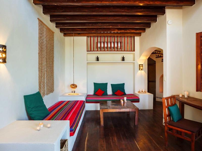 Coin chambre d'hôtel cosy avec poutres en bois, canapé, table en bois et accents colorés.