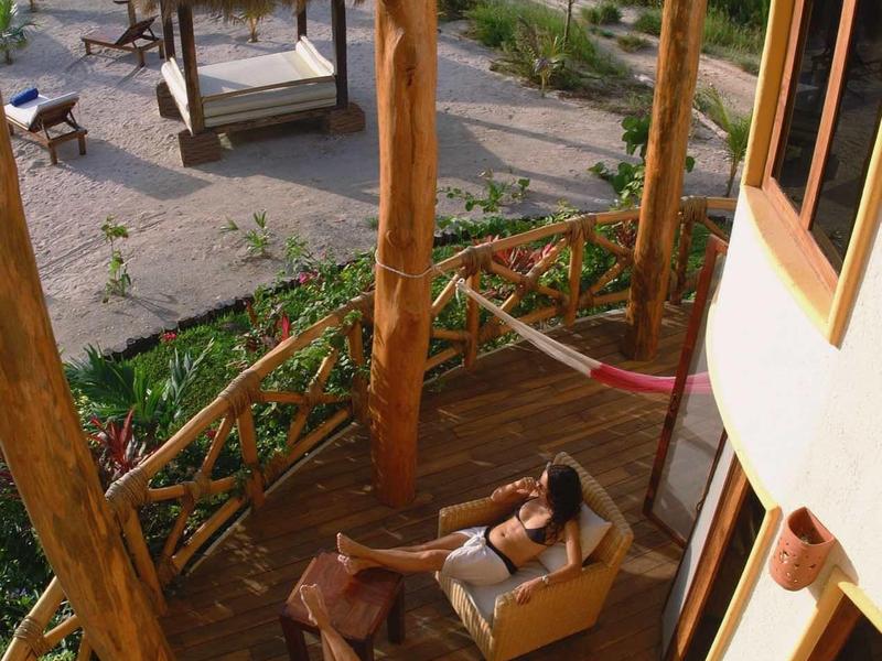Balcon avec sièges et personne face à la plage et la mer au coucher du soleil.