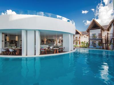 Moderner Hotelbereich mit großem Pool und Gebäuden im tropischen Stil unter blauem Himmel.