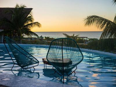 Zwei Stühle im Pool mit Blick auf Palmen und Sonnenuntergang am Meer.