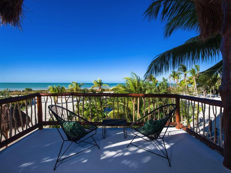 Balcon avec chaises donnant sur la mer, ciel bleu et palmiers
