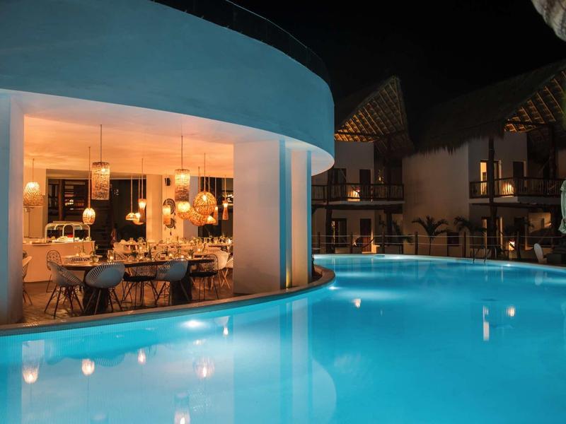 Piscine éclairée la nuit devant un restaurant d'hôtel avec de grandes fenêtres.