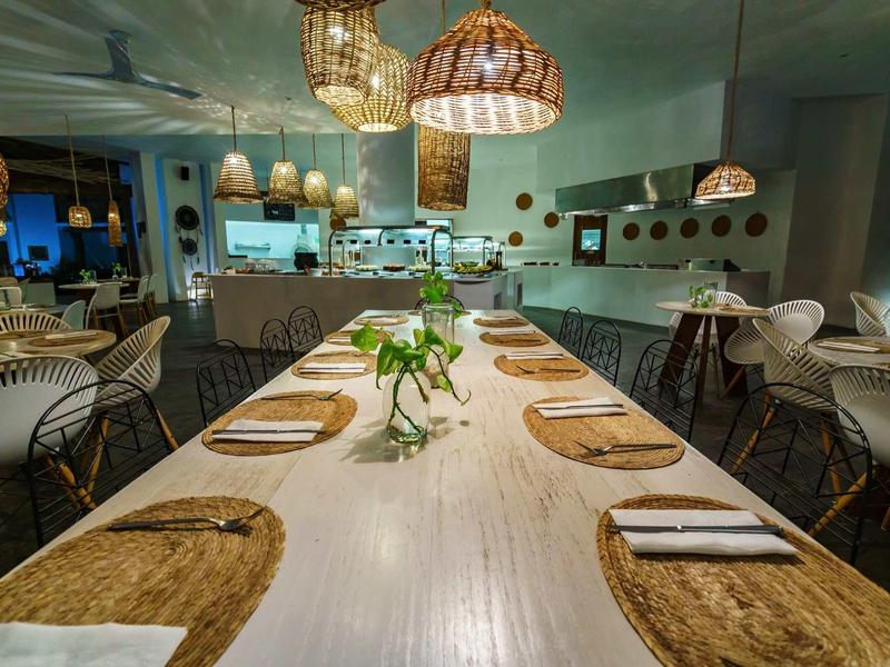 Restaurant moderne avec une longue table dressée et des lampes suspendues dans une ambiance chaleureuse.