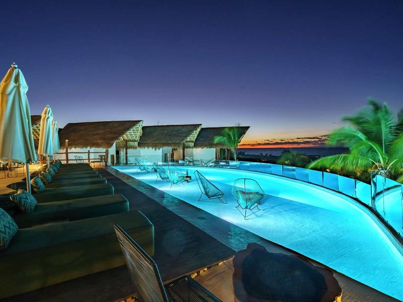 Espace piscine moderne avec chaises longues et abris au coucher du soleil.