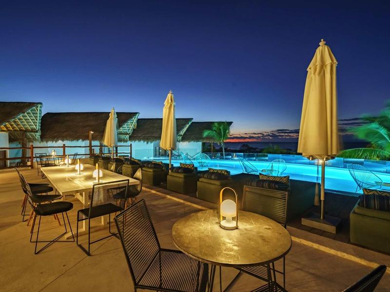Terrasse d'hôtel avec sièges et piscine éclairée la nuit sous un ciel dégagé.