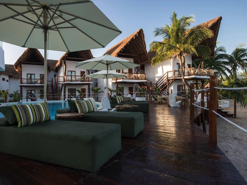 Espace piscine luxueux avec transats, parasols et villas tropicales en arrière-plan.