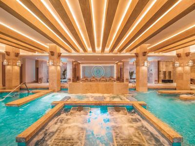 Luxuriöser Wellnessbereich mit beleuchtetem Pool, Säulen und Holzdeck in warmem Licht.