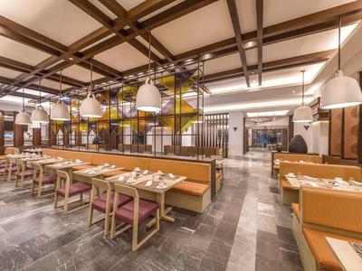 Großes, helles Restaurant mit Holzdecke, Sitzbänken, Holztischen und modernem Beleuchtungskonzept.