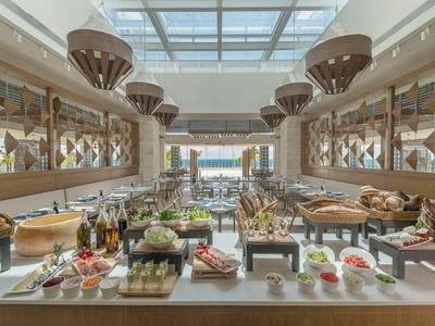 Großzügiges Buffet mit vielfältigen Speisen in hellem, modernem Raum mit großen Fenstern.