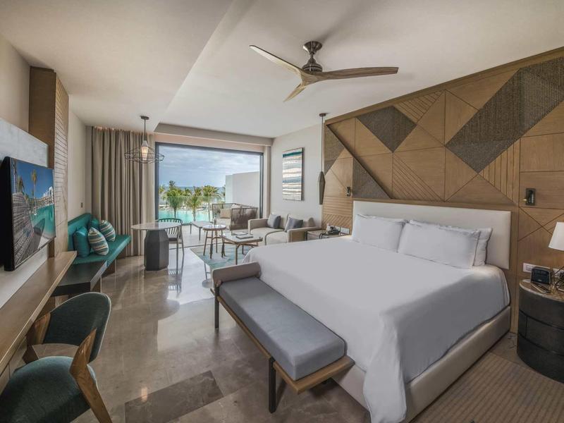 Modernes Hotelzimmer mit großem Bett, Küchenzeile, Balkon und hellem, minimalistischem Design.