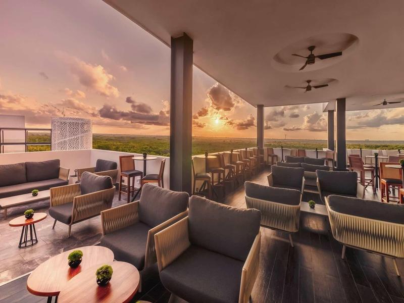 Dachterrasse mit Sofas, Tischen und Stühlen bei Sonnenuntergang, offener Blick auf Himmel und Landschaft.