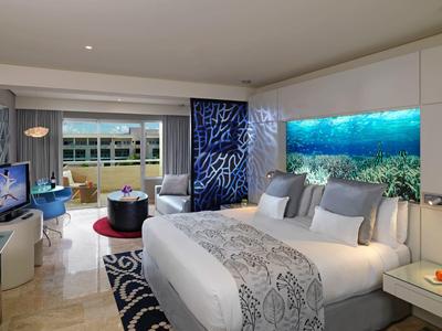 Modernes Hotelzimmer mit großem Bett, Meerwasser-Aquarium als Wanddekoration und Blick auf Balkon.