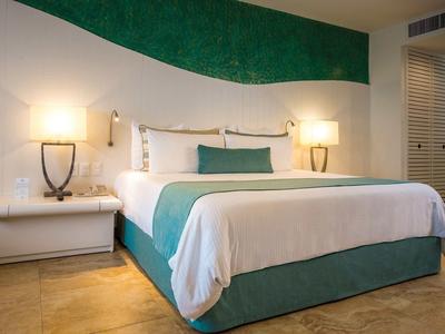 Modern hotelkamer met groot bed, groene accenten en warme wandverlichting.