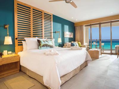 Modern hotel room with king-size bed, wooden furniture, and ocean view through large windows.