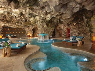 Zona piscina di lusso all'interno di una grotta naturale con comodi posti a sedere e luce calda.