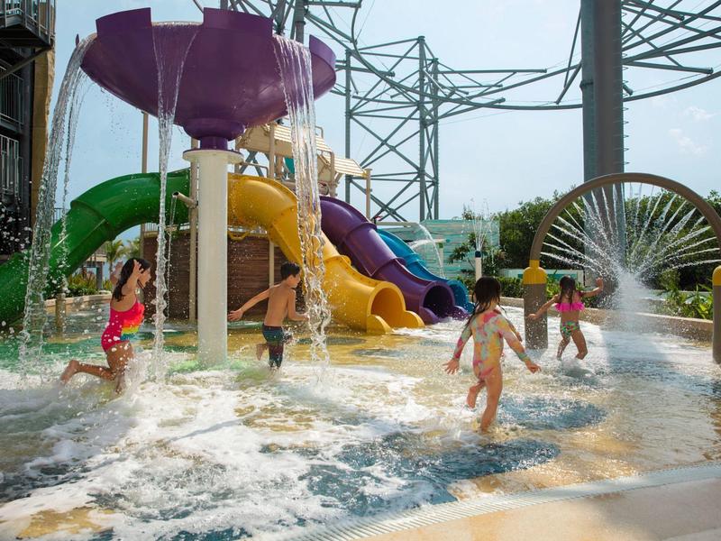Bambini che giocano in un parco acquatico con scivoli colorati e giochi d'acqua.