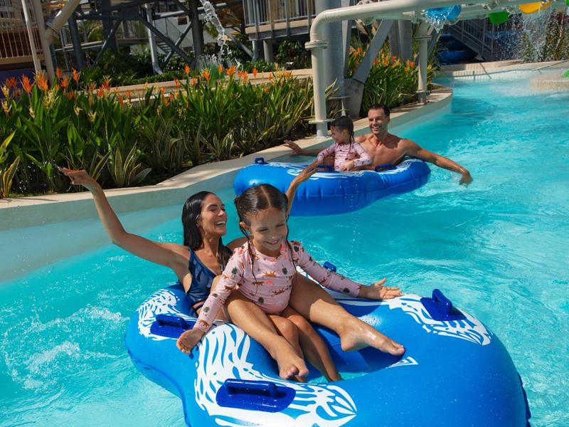 Famiglia che si rilassa su ciambelle gonfiabili blu in un parco acquatico, bambini davanti.