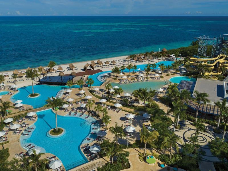 Grande piscina dell'hotel con bacini collegati, palme e vista su una spiaggia di sabbia.