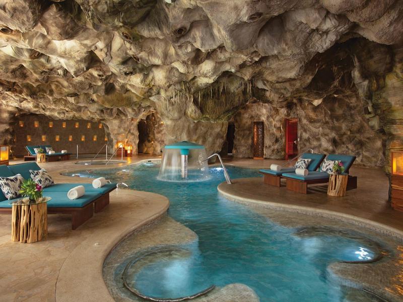 Zona piscina di lusso all'interno di una grotta naturale con comodi posti a sedere e luce calda.