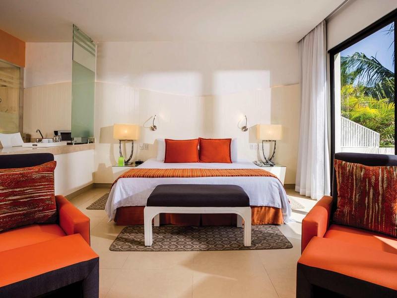 Camera d'hotel moderna con grande letto, accenti rossi e vista sulle piante tropicali.