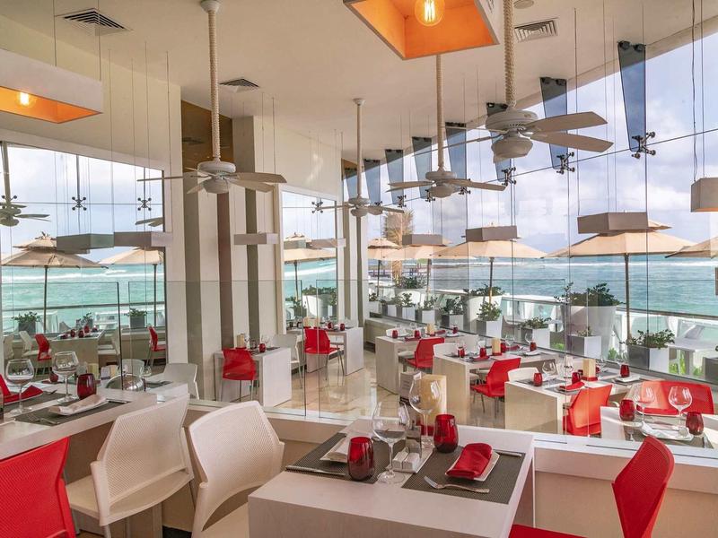 Ristorante luminoso e moderno con grandi finestre che si affacciano sulla terrazza e sul mare.