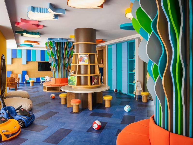 Área de juegos colorida con madera, cojines y juguetes para niños en un espacio interior de hotel.