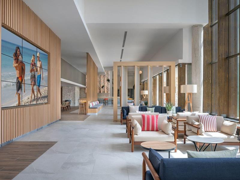 Área de salón de hotel moderno con sofás, acabados en madera y gran foto de playa en la pared.