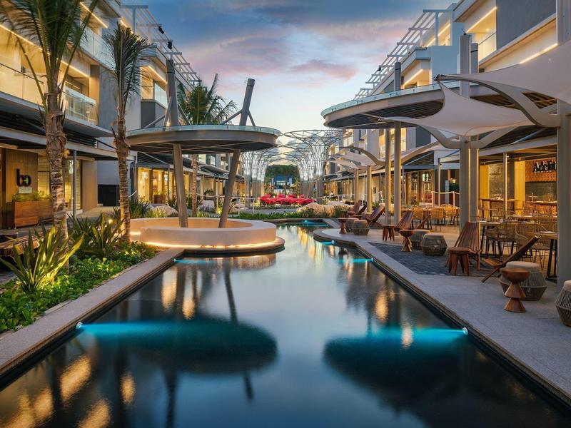 Piscina larga con sombrillas y sillas en un área exterior de hotel al atardecer.
