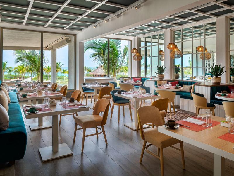 Restaurante moderno de hotel con vista al mar, decoración elegante y muebles de madera estilizados.