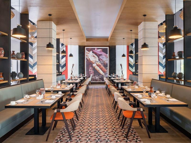 Restaurante moderno con sillas Poncho, largas filas de mesas y suelo con patrón en el hotel.