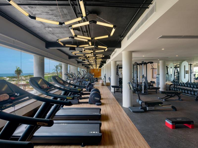 Gimnasio moderno con cintas de correr junto a grandes ventanales con vista al mar