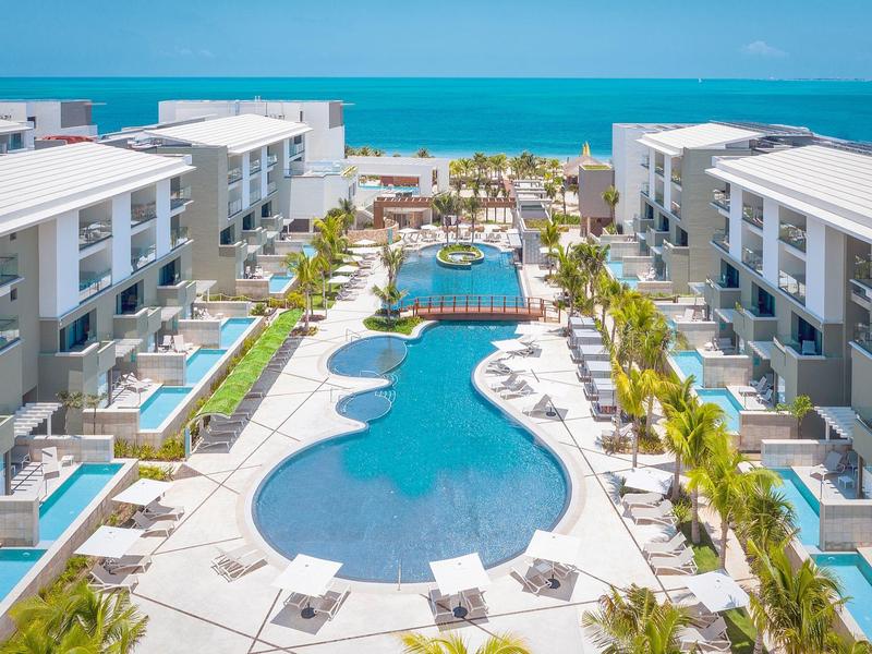 Complejo hotelero moderno con una gran piscina y vistas al mar azul al fondo.