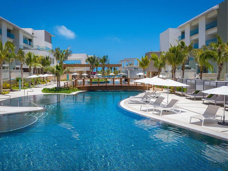 Gran piscina exterior entre dos edificios del hotel con tumbonas y sombrillas bajo cielo azul.