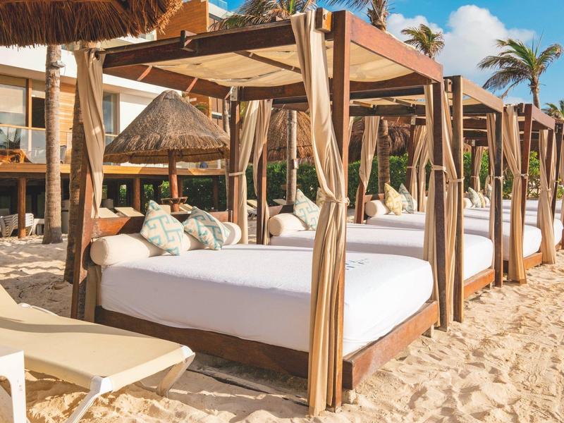 Spiaggia con letti a baldacchino bianchi e palme davanti a un hotel