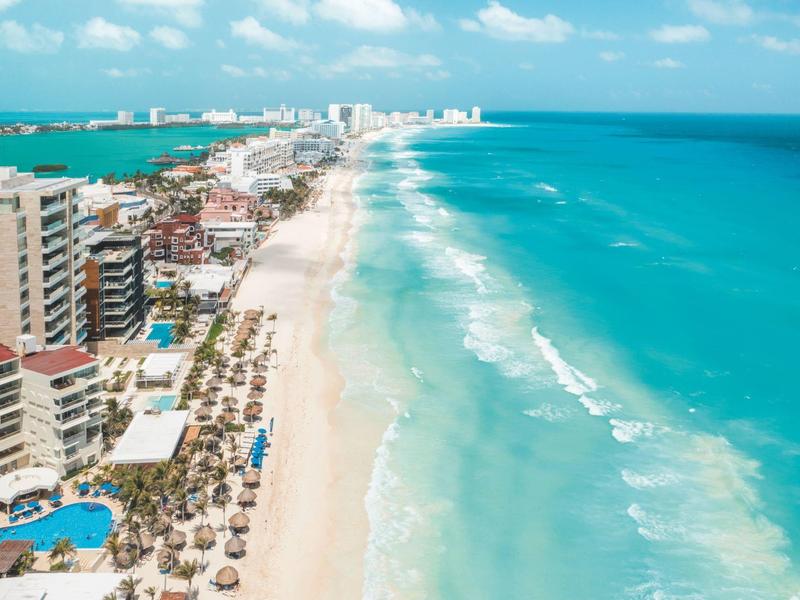 Lunga spiaggia sabbiosa con hotel, lettini e ombrelloni sul mare turchese.