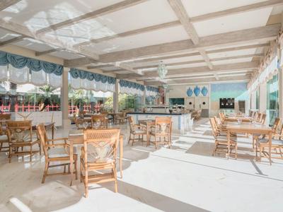 Heller, offener Restaurantbereich mit Holzstühlen, Tischen und großen Fenstern für viel Tageslicht.