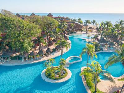 Großer Hotelpool mit Palmen und Blick auf den Strand und das Meer im Hintergrund.