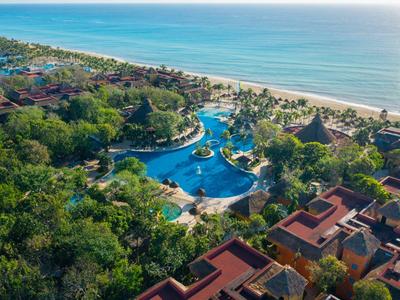 Resort con varias piscinas junto a la playa, rodeado de mucha vegetación y edificios.